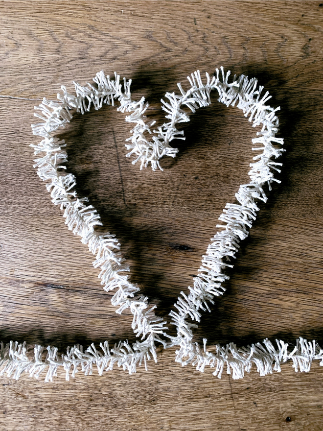 Plain Cotton Strinsel (plastic free string tinsel) forming a white heart on an oak background