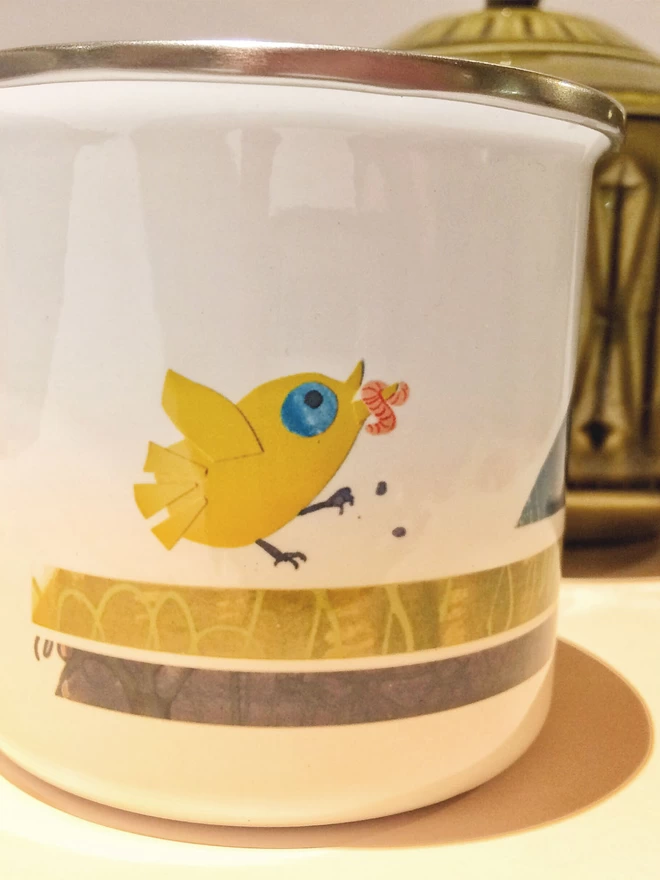 Detail of a white enamel mug decorated with a yellow baby bird with a pink worm in its beak