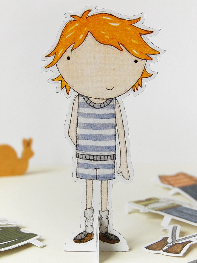 A paper doll wearing a striped vest stands on a white desk.