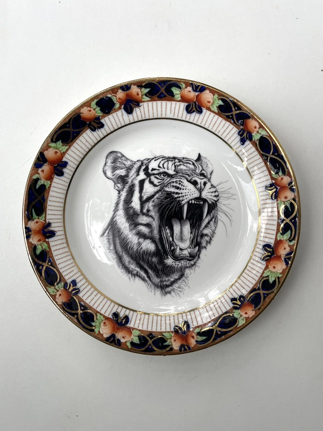 a vintage plate with an ornate border, in the centre of the plate is a vintage style black and white illustration of a tiger roaring