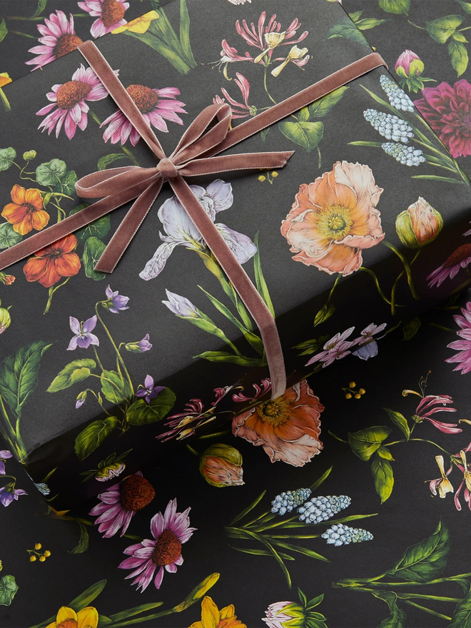 bountiful blooms floral gift wrap sheet. a box wrapped in black illustrated floral gift wrap with a purple ribbon.