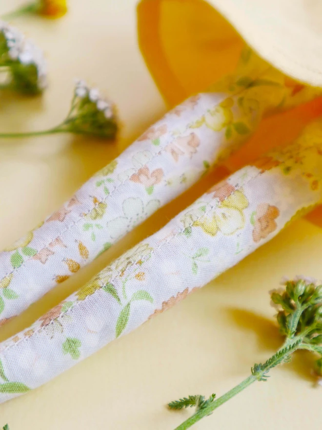 Handmade heirloom cloth doll with freckled face, red corduroy hair in two buns, floral leggings, and a soft yellow dress, styled on a neutral background with delicate wildflowers.