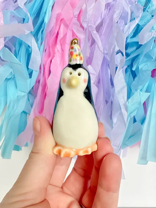 Handmade Porcelain Party Penguin Topper, held by hand above party decorations. 