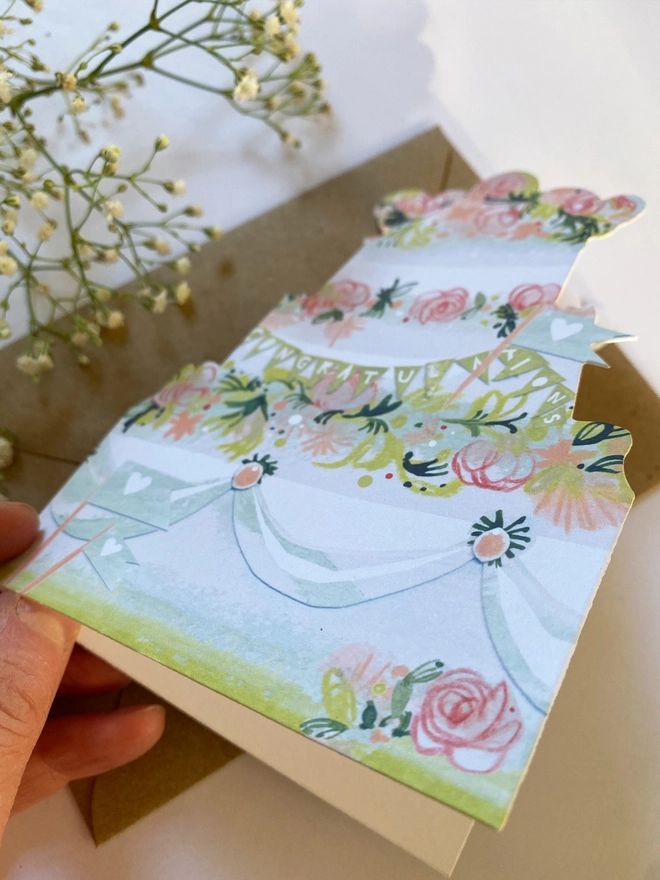 Esther kent illustrated greetings card in the shape of a tierd cake decorated with pink flowers and greenery. 