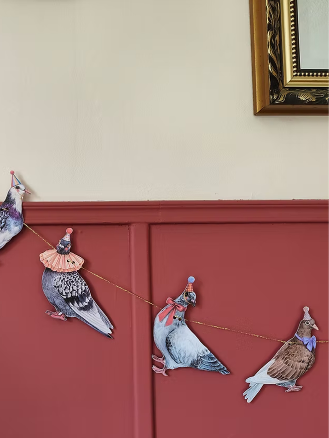 party pigeons circus garland. a string of paper pigeons in party and circus hats hung up on a wall.