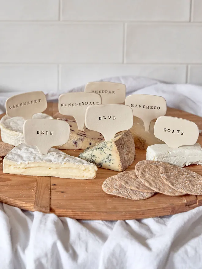 Ceramic cheese makers a group shoot embedded in a cheese platter. They read: Chedder, Blue, Manchego, Brie, Wensleydale, camembert