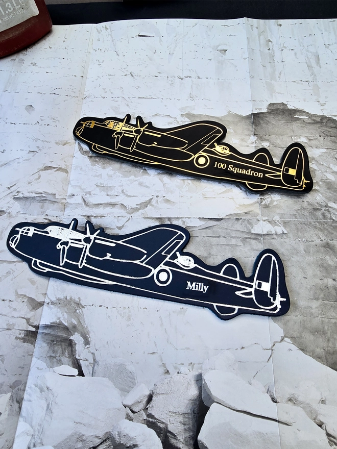 two leather warplane bookmarks of a Lancaster bomber plane in black and gold leather and blue and silver leather personalised with one hundred squadron and Milly on a map of the arctic