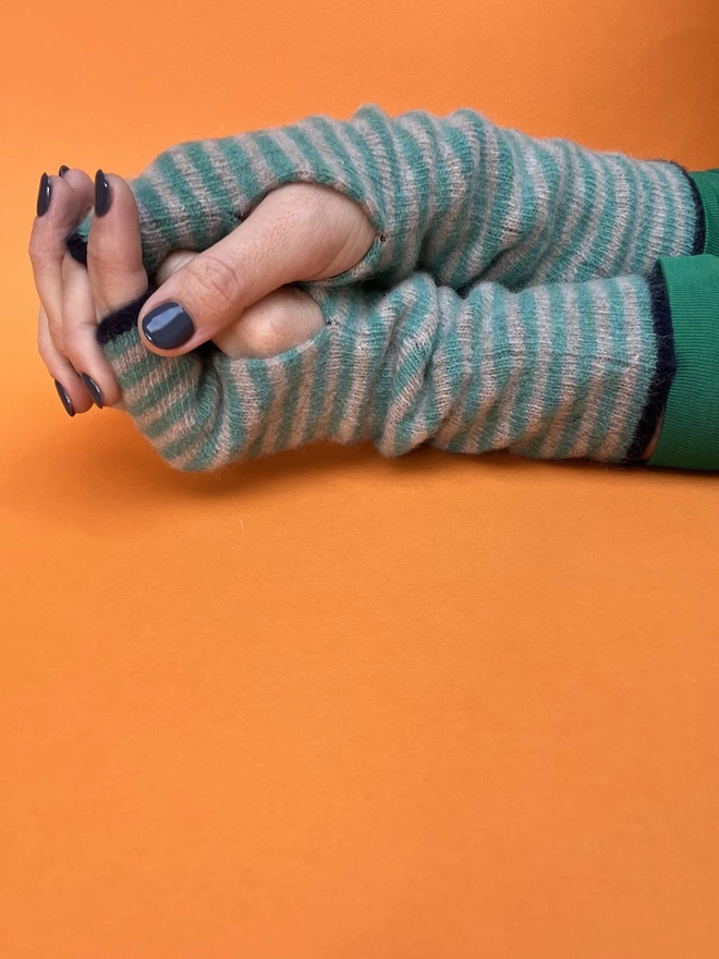 Knitted striped wristwarmers shown on hands on an orange background