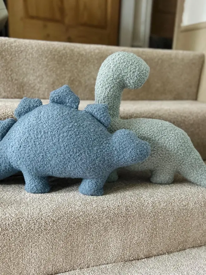 boucle dinosaur pillows. a blue stegosaurus and green t rex cushion photographed on stairs.