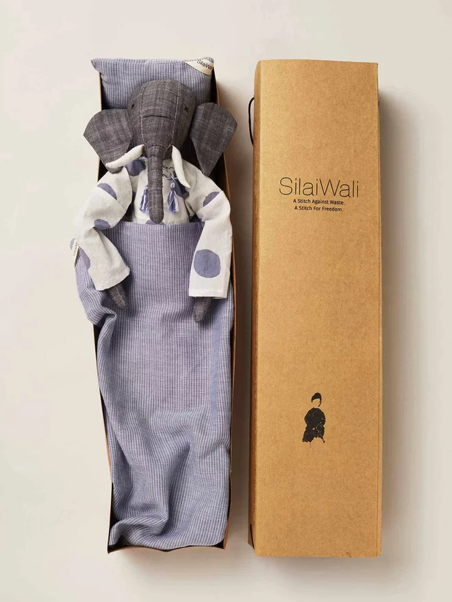 Grey elephant stuffed doll inside a cardboard box with pinstripe navy sheet covering half of his body 