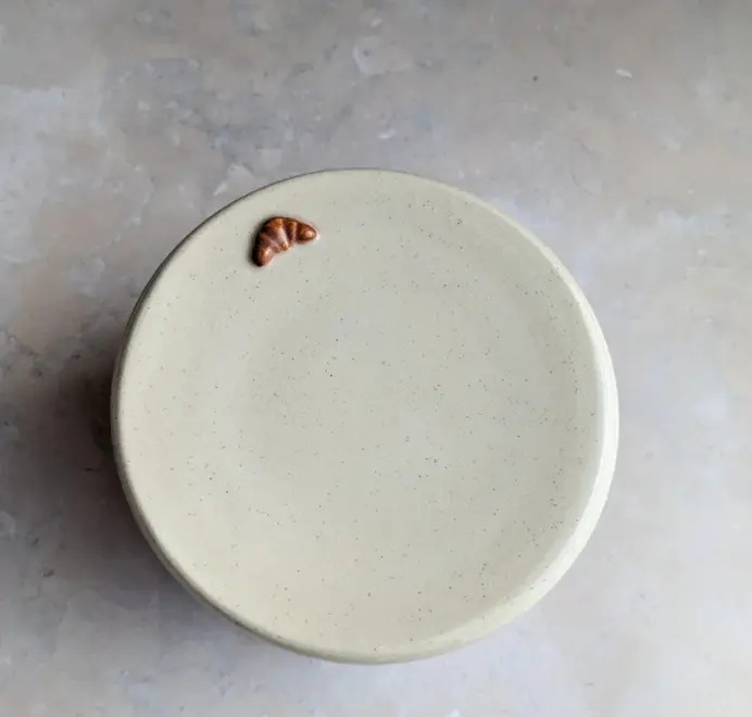 Birds eye view of the Croissant Butter Crock in vanilla bean glaze with a small croissant design on the front, set against a clean white marble background.