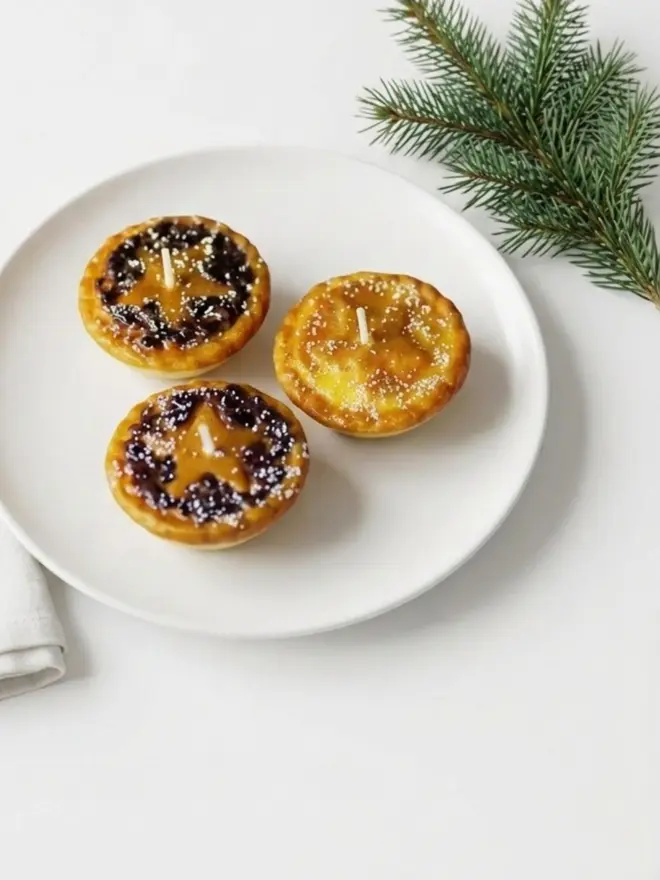 The mince pie candle. three candles shaped like mince pies on a white cake stand.