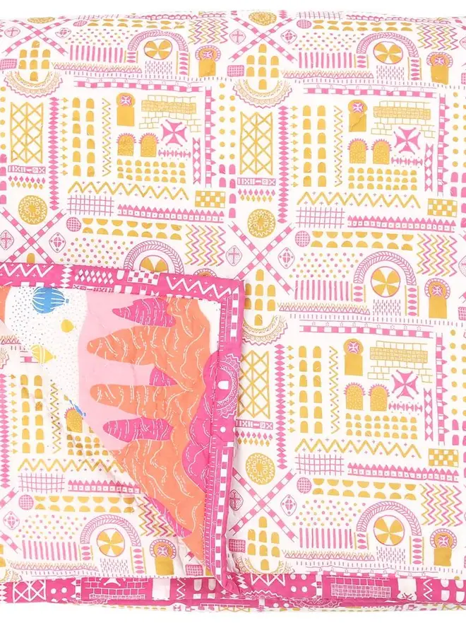 Fairy Chimney Quilt, a pink and yellow quilt sitting on a bed in a bedroom. 