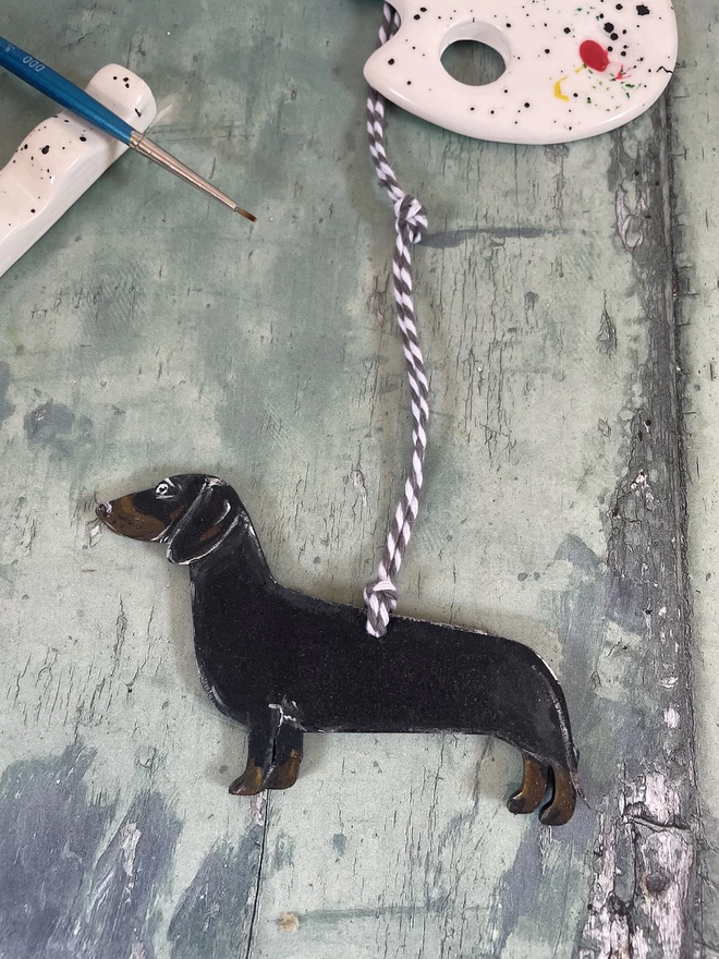 A dachshund memory decoration next to a paint palette and paint brush 