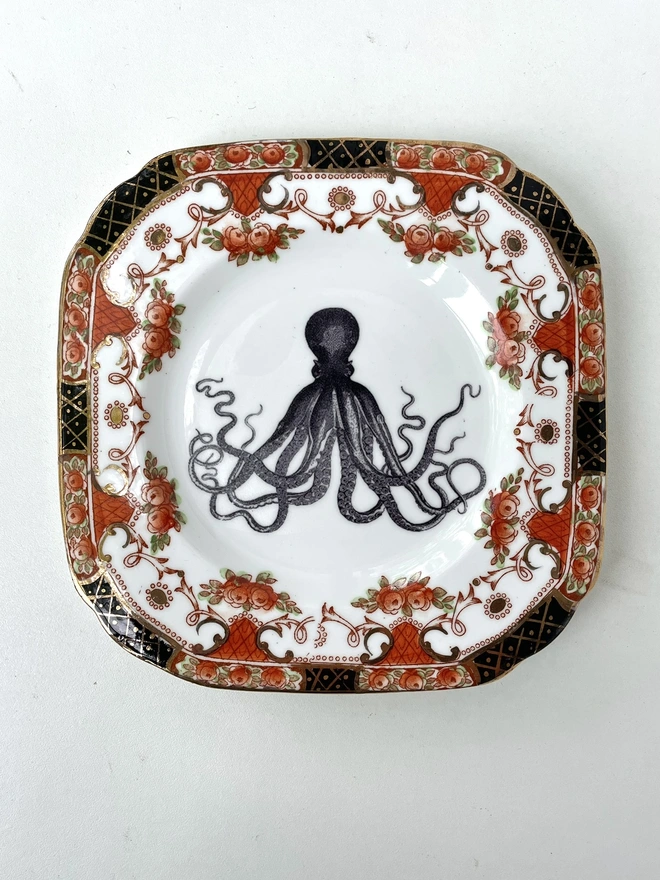 vintage plate with an ornate border, with a printed vintage illustration of an octopus in the middle 