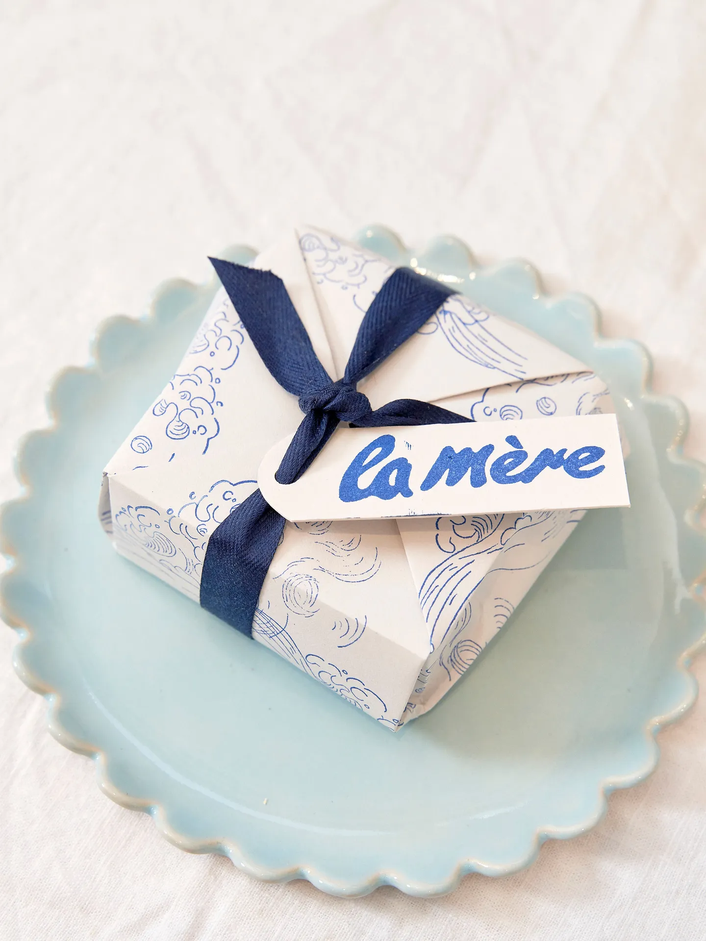 white paper box with blue ribbon and 'la mere' tag, on blue plate