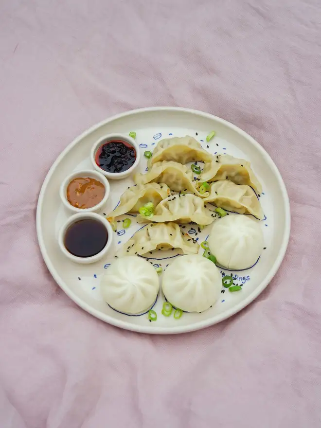 Dumplings Dippy Dinner Plate, a dipping plate sitting on a purple bed cloth. It is covered in dumplings and dipping sauces. 