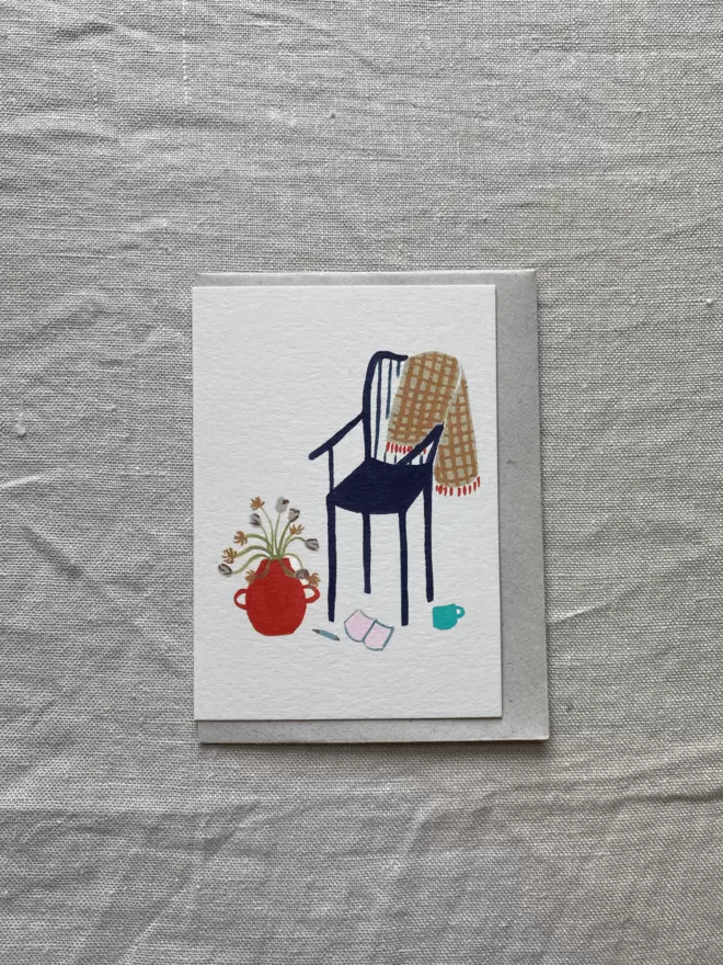 greetings card with a chair, book and throw on it. An cosy afternoon set up.
