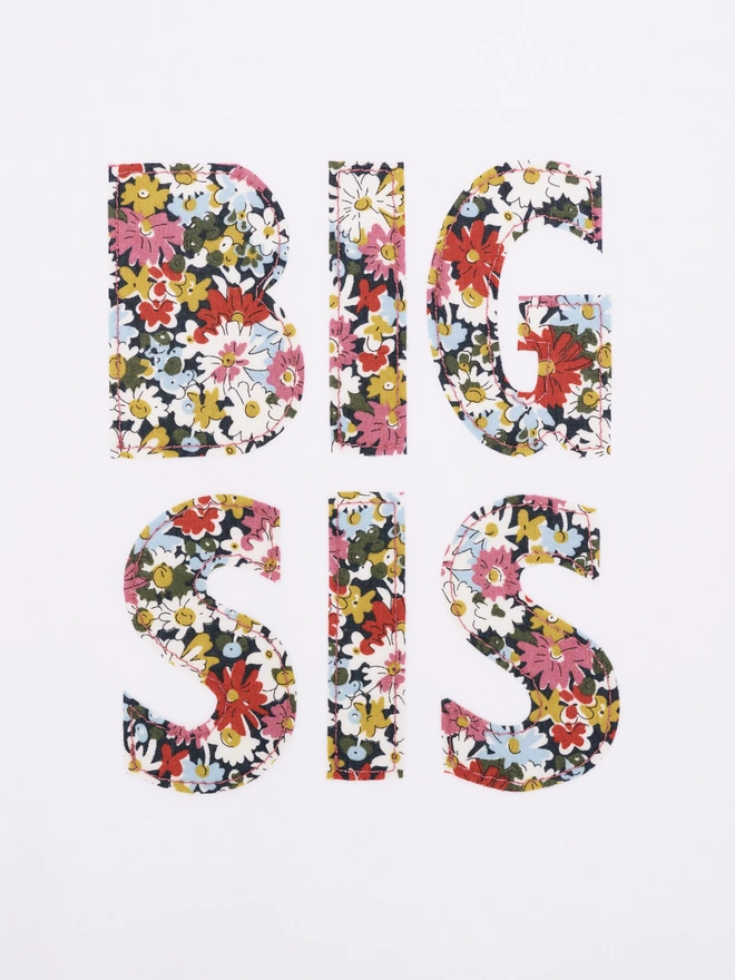 a close up of a white t-shirt that says Big Sis in the front in floral print. the letters are appliquéd onto the front