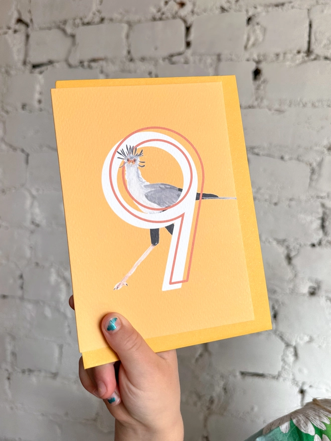 Bright yellow card with an illustration of a secretary bird and a big white number 9, with a yellow envelope