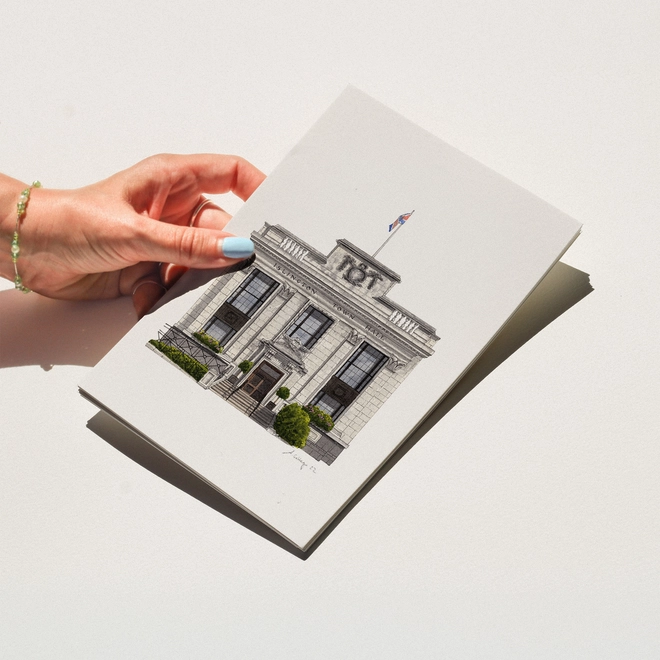 A hand with blue nail polish holding a print featuring an illustration of Islington Town Hall against a white background.