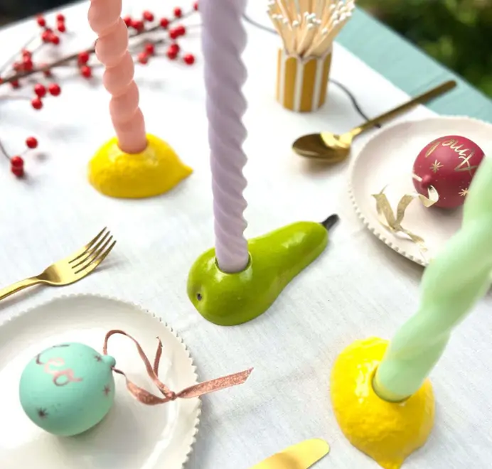 Candles placed in yellow lemon candlestick holders displayed on a table alongside green candlestick holders. 