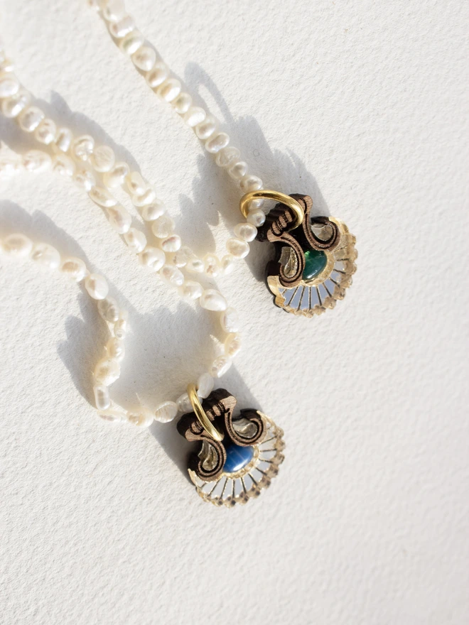 Pearl necklace with a shell shaped gold pendant & gemstone on a white background