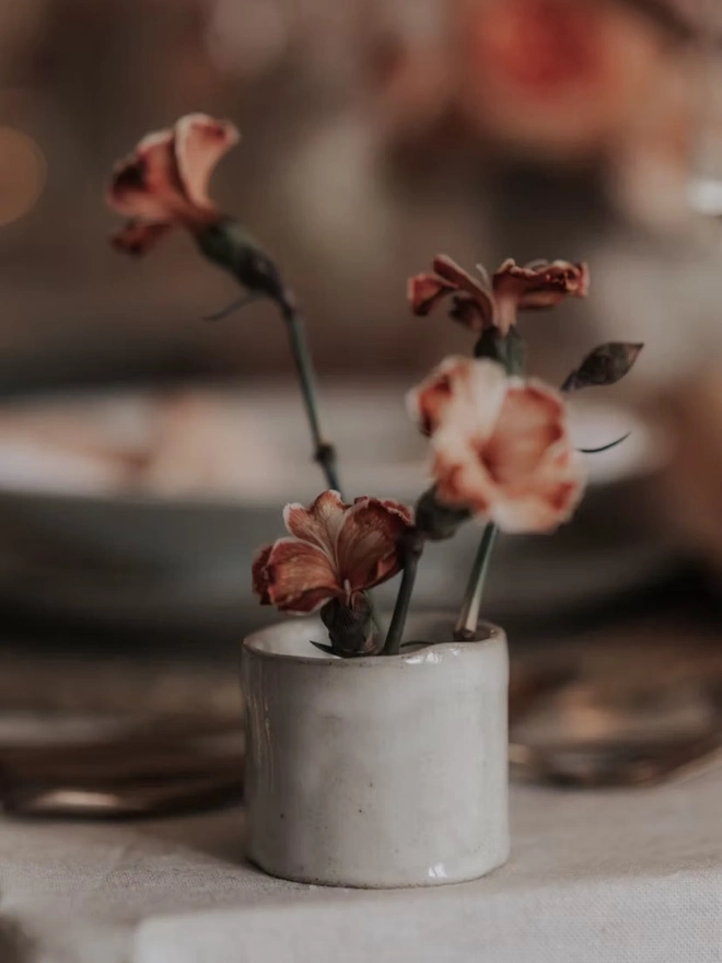 Ikebana, ceramic vase pictured with pink flowers on a ledge. 
