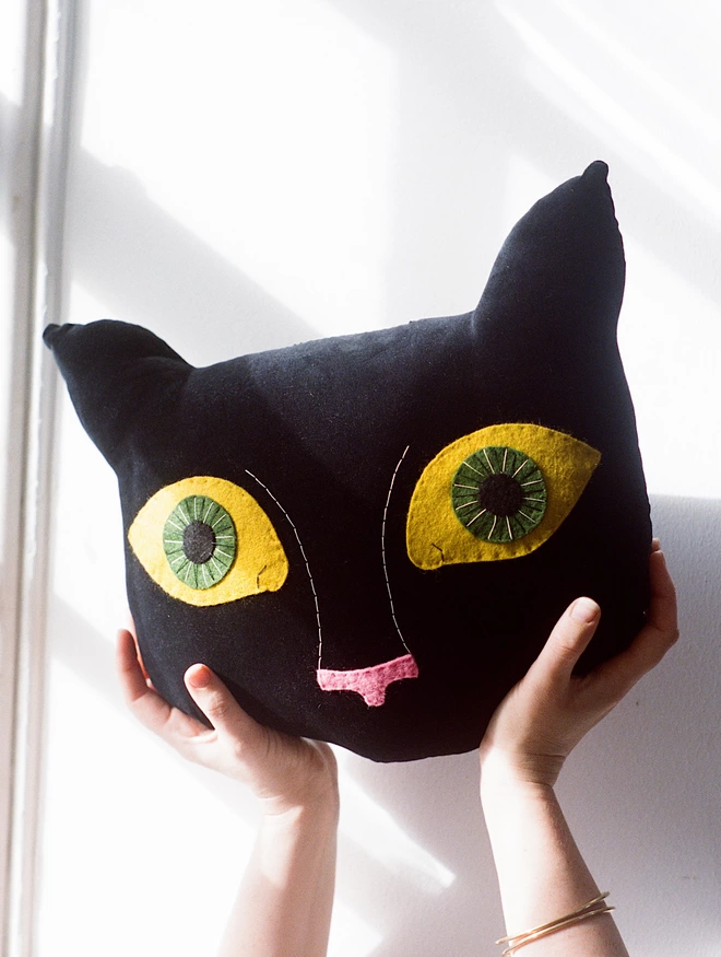 black velvet cat cushion with big green and yellow eyes 
