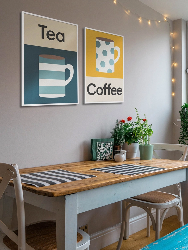 Two illustrated wall prints featuring a mug of coffee and tea hanging on cafe wakk