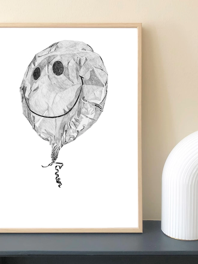 Art print of a hnad drawn crumpled smiley balloon displayed in a frame