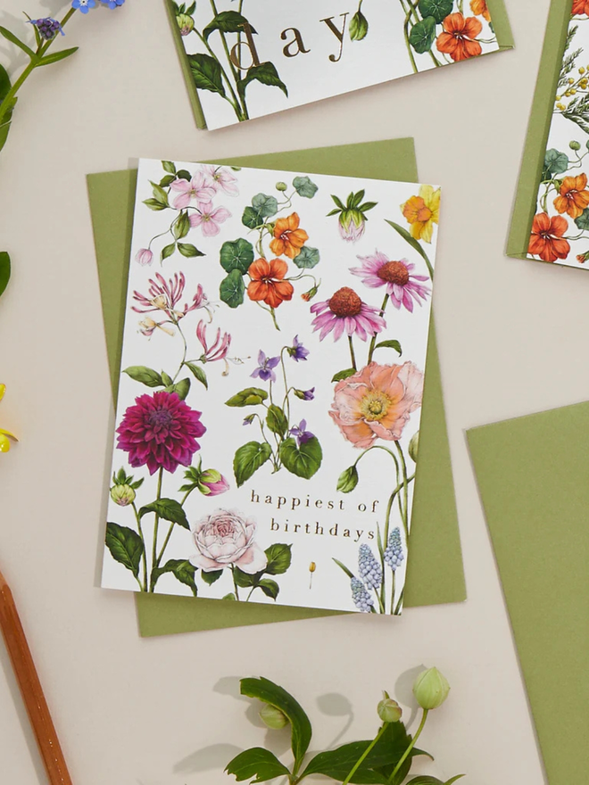 'Happiest Of Birthdays' Illustrated Floral Card. a white floral card and green envelope photographed against a plain background.