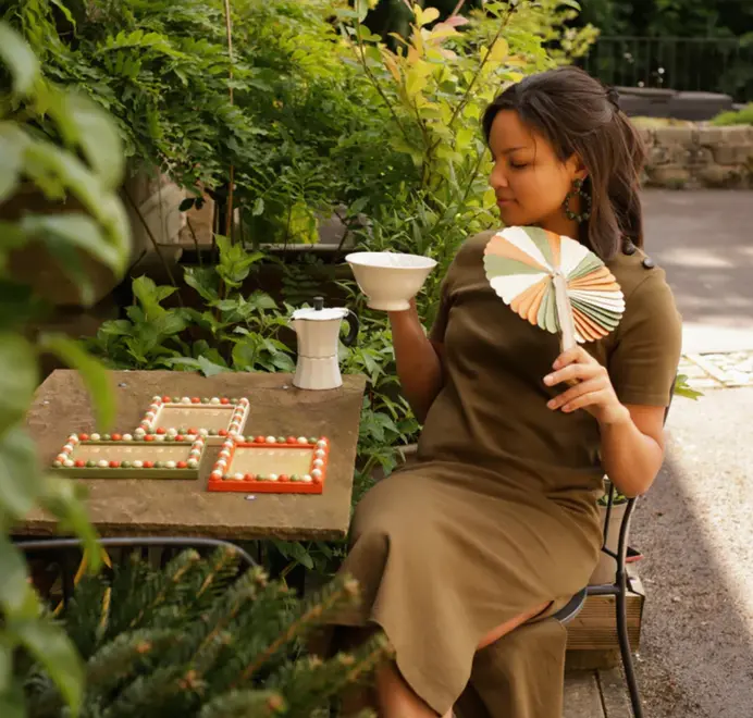 white orange and green bobbin frames next to woman holding hand fan in matching colours