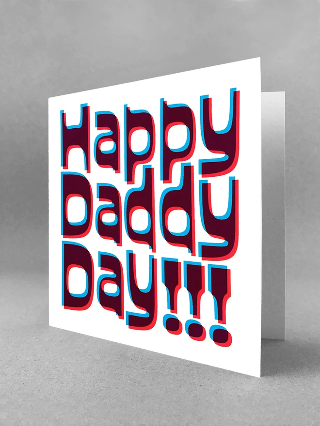 Happy Daddy Day printed in magenta and cyan blue ink, a slight overlapped design to create this retro jolly card. Stood slightly open on a white studio background.