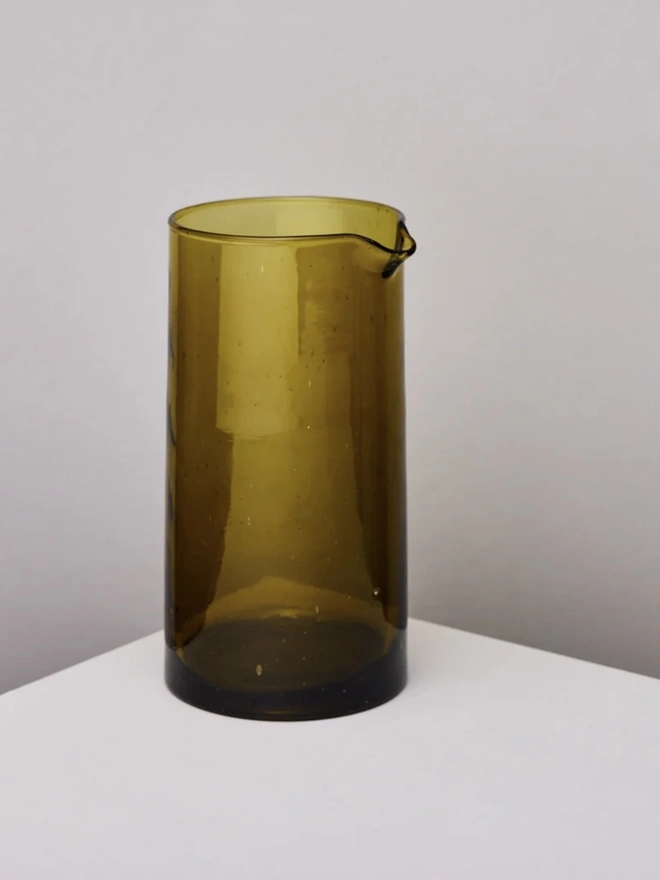 Glass Carafe, a large amber glass jug sitting on a plain counter top against a grey backdrop. 
