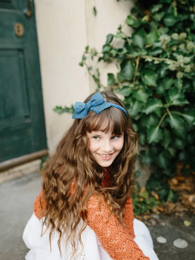 Alice Band with large bow in blue gingham on girl sitting on a step outside her house 