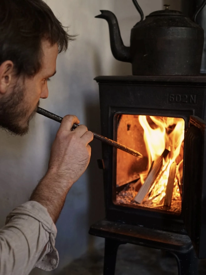 Fire Blower, a man using a metal fire blower to light a fire. 