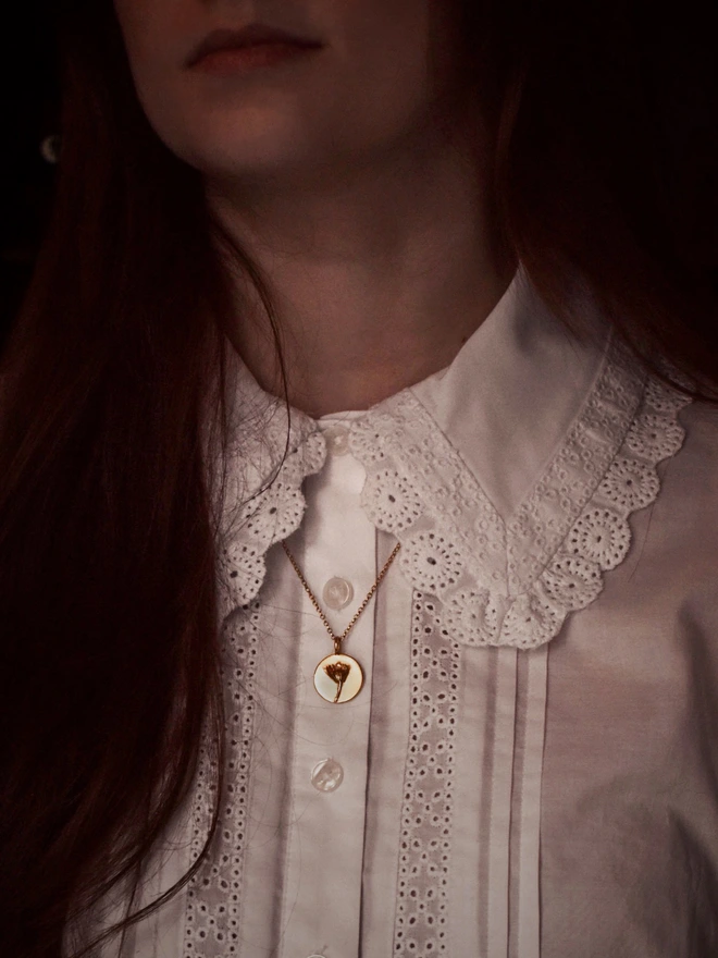 Front view of a Gold Daisy Coin Charm representing new beginnings in the language of flower worn by a model