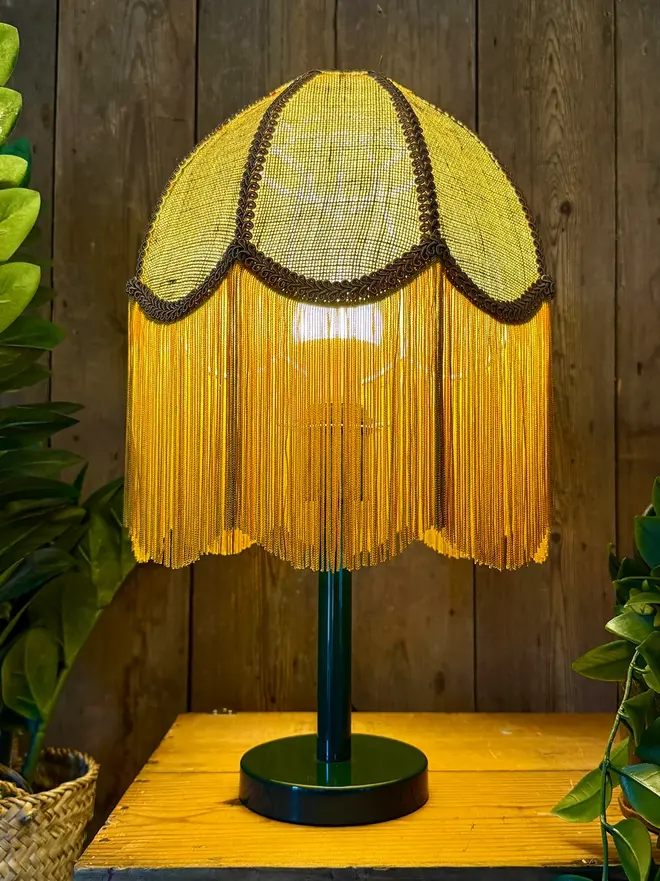 Fringed Hessian Lampshade In Pickle Green And Antique Gold, in a room. 