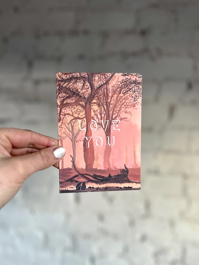 a greetings card featuring an illustration of a sunset through the trees with the text “love you”