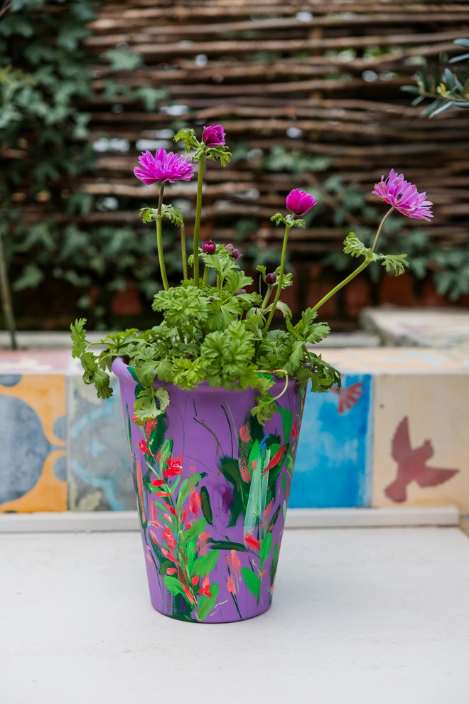 Unique hand-painted terracotta pot featuring twizzle coral flowers on a purple background