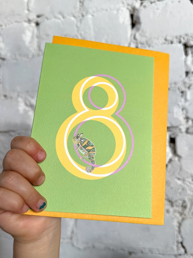 a bright green card with a big yellow number 8 and an illustrated chameleon with a bright yellow envelope