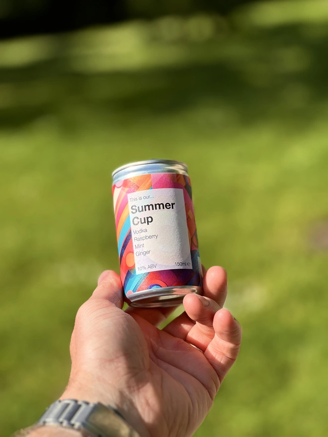 Can of Summer Cup, held in a hand, with a grass backdrop