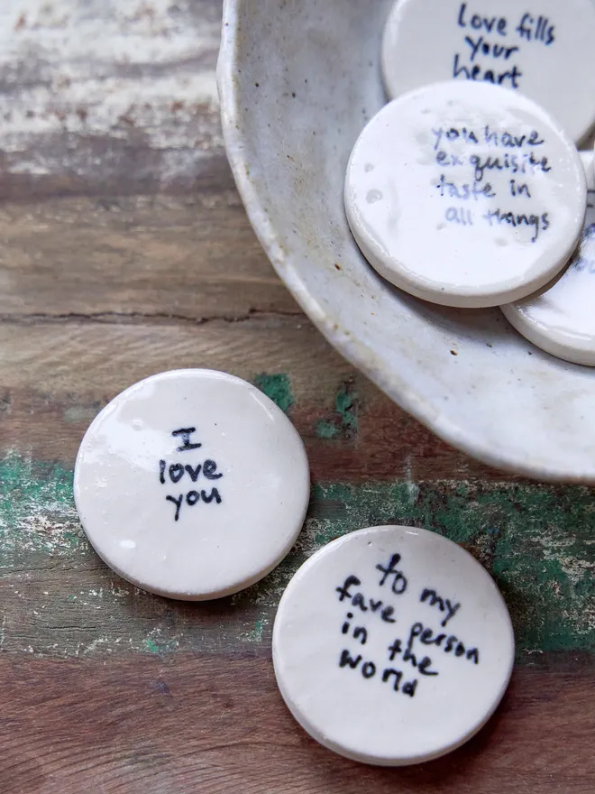 Small ceramic love token. A group of ceramic love tokens in a ceramic bowl and some on a wooden surface.