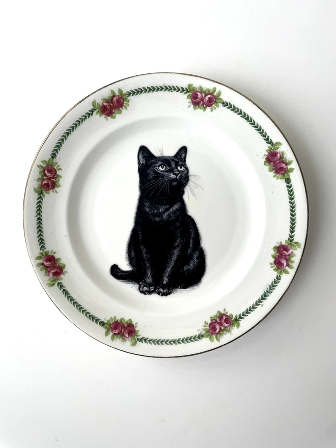 a vintage plate with an ornate border, in the centre of the plate is a vintage style black and white illustration of a black witch's cat
