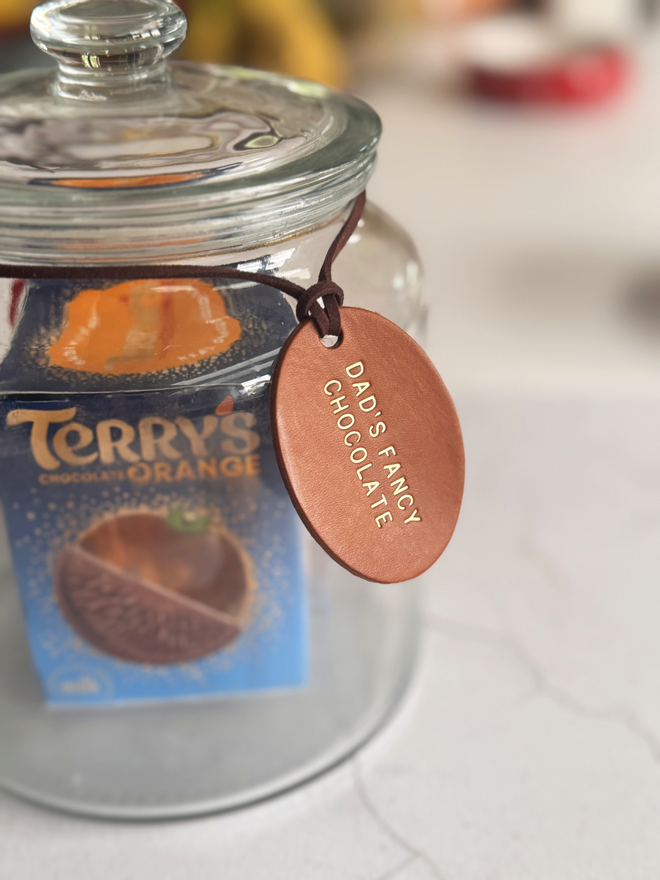 a glass jar with chocolate in, a leather label with 'Dad's Fancy Chocolate' stamped on the brown tag with gold writing.