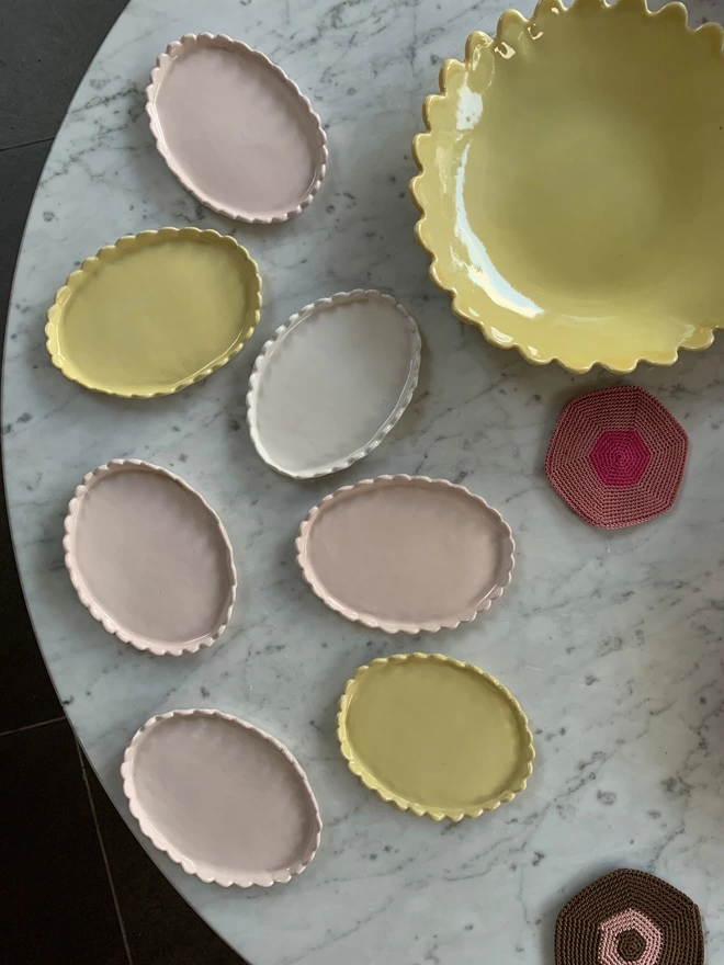 a tabletop with a group of scalloped edge butter dishes in yellow, white and blossom pink