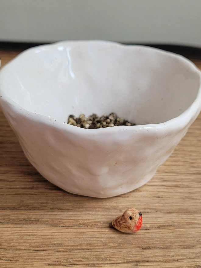 white pottery pepper pinch pot with course ground pepper inside and tiny ceramic robin bired in the foreground