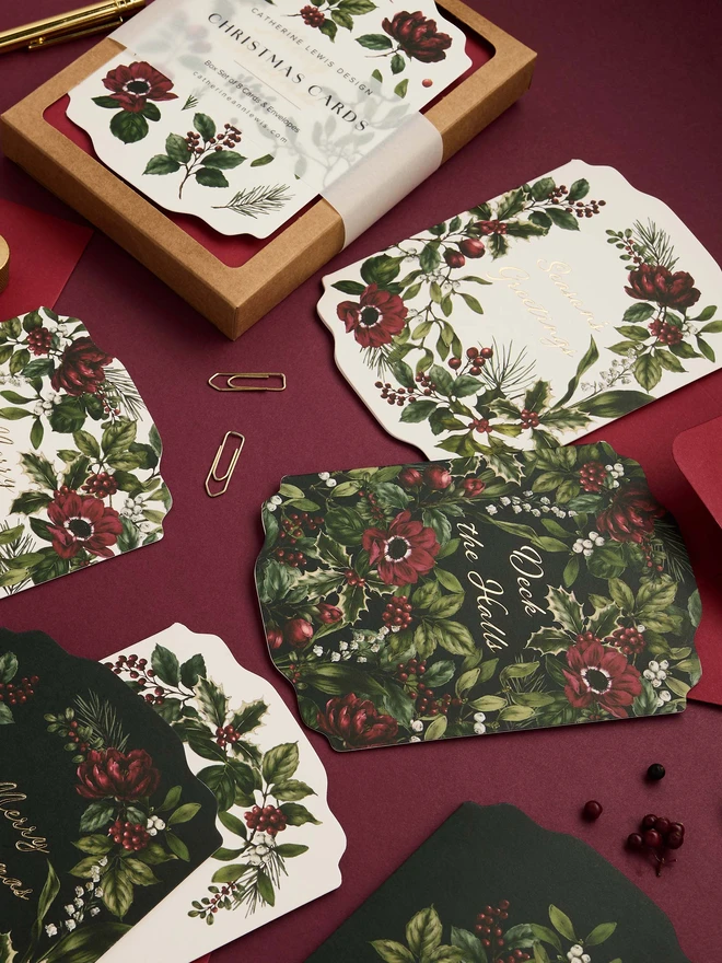 Box of 8 cards, with red envelopes. gold foil and die-cut shape cards with greens and red botanicals