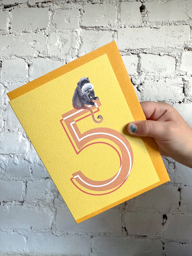 bright yellow card featuring a big orange number 5 and an illustration of an emperor tamarin with a bright yellow envelope